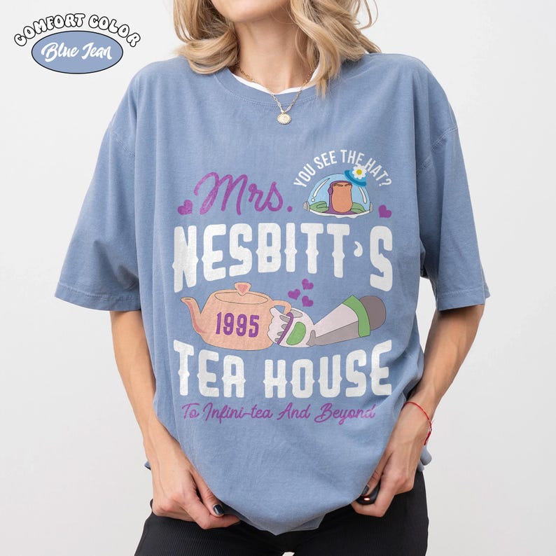 May include: Blue jean Comfort Colors t-shirt with a graphic design. The design includes the text "Mrs. Nesbitt's Tea House" with a teapot, the year 1995, and the phrase "To Infini-tea And Beyond".