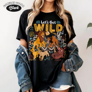 May include: Black t-shirt with the text "Let's Get WILD" and a colorful graphic featuring characters from The Lion King. The graphic includes lions, a warthog, and other characters. The shirt is labeled "Comfort Color Black".