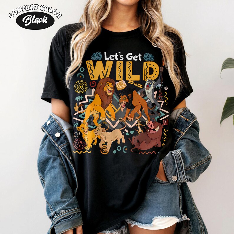 May include: Black t-shirt with the text "Let's Get WILD" and a colorful graphic featuring characters from The Lion King. The graphic includes lions, a warthog, and other characters. The shirt is labeled "Comfort Color Black".