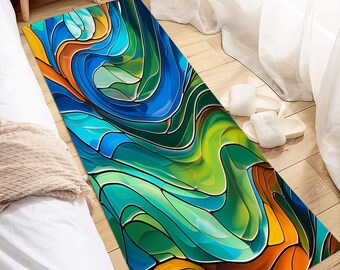 Könnte beinhalten: Ein rechteckiger Teppich mit einem Buntglasdesign. Der Teppich weist fließende Muster in Blau-, Grün-, Orange- und Gelbtönen auf. Der Teppich liegt auf einem Holzboden neben einem Bett.