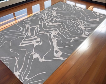 Puede incluir: Una alfombra rectangular gris con un diseño abstracto blanco. La alfombra presenta un patrón lineal y fluido en su superficie. La alfombra está colocada sobre un suelo de madera. La habitación tiene grandes ventanas.