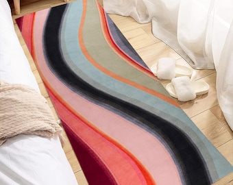 Könnte beinhalten: Ein rechteckiger Teppich mit wellenförmigem Muster in Rot, Rosa, Schwarz, Blau und Grau. Der Teppich besteht aus einem weichen Material und liegt auf einem Holzboden. Das Design erzeugt ein wellenartiges Muster.