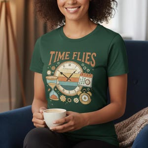 May include: A dark green t-shirt with the words "TIME FLIES" above a clock, hourglass, and calendar graphic. The clock has a retro design with orange, yellow, and blue stripes. The person is holding a white mug.