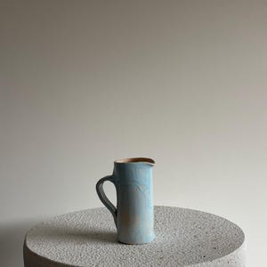 Op de afbeelding: Een witte keramische mok met een zwarte handgreep en de tekst "But First, Coffee" in handschriftstijl. De mok staat op een wit oppervlak. De mok is ongeveer 10 cm hoog.