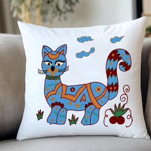Puede incluir: Un cojín cuadrado blanco con un diseño de gato azul estilizado, con detalles en naranja y flores. El gato tiene una cola larga y está rodeado de hierba verde y nubes azules. Cojín decorativo.