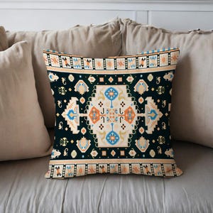 May include: Decorative throw pillow with a dark teal background and a central geometric design in cream, orange, and blue. The pillow features a border with repeating patterns in shades of tan and orange, adding a touch of bohemian flair.