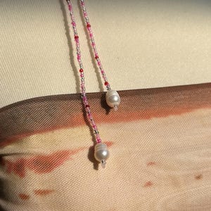 Puede incluir: Un top sin tirantes con un degradado en tonos beige, marr&oacute;n y naranja, acentuado por dos delicados cordones de cuentas. Cada cord&oacute;n est&aacute; compuesto por peque&ntilde;as cuentas rosas, rojas y plateadas, terminando en una perla de agua dulce blanca.