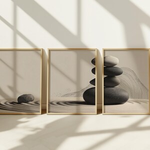 Könnte beinhalten: Drei gerahmte Drucke mit Zen-Garten-Designs. Die Drucke haben eine neutrale Farbpalette mit beigen Hintergründen und goldenen Rahmen. Ein Druck zeigt einen einzelnen Stein, ein anderer einen Steinhaufen und der dritte ein Stein- und Sandmuster.