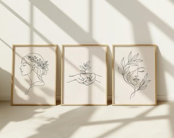May include: Three framed art prints with minimalist line drawings. The prints feature a woman's profile with floral accents, hands holding a plant, and a face with leaf details. The frames are a light wood color, and the background is a neutral beige.