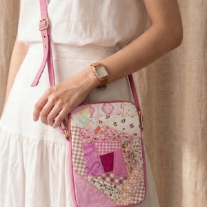 May include: A rectangular crossbody bag featuring a patchwork design of various pink, white, and floral fabric patterns. The bag includes a matching pink adjustable shoulder strap with gold-toned metal hardware and a zipper closure along the top edge.