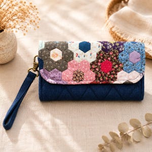 Può includere: Un portafoglio trapuntato con un design floreale patchwork nei toni del rosa, blu, viola e marrone. Il portafoglio ha una base blu navy con un cinturino da polso e una chiusura in metallo.