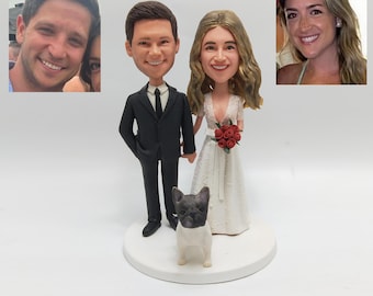Op de afbeelding: Een taarttopper voor een bruiloft met een bruid en bruidegom figuur, een kleine hond en twee kleine foto's. De bruidegom draagt een zwart pak en de bruid een witte jurk met een boeket rode rozen. De hond is zwart en wit.