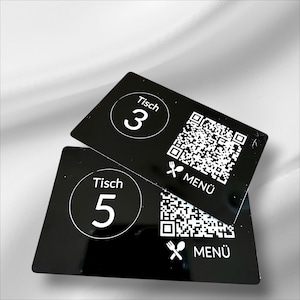 Puede incluir: Dos tarjetas de mesa rectangulares negras con texto blanco y un código QR. Una tarjeta dice "Tisch 3" y la otra "Tisch 5". Ambas tarjetas tienen la palabra "MENU" y un icono de tenedor y cuchara.