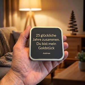 Könnte beinhalten: Eine quadratische Metalldose mit abgerundeten Ecken, einem schwarzen Deckel und goldener Aufschrift: 25 glückliche Jahre zusammen. Du bist mein Goldstück. Andreas. Der Behälter hat einen silberfarbenen Metallrand und eine glatte Oberfläche.