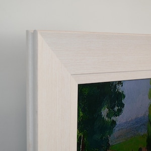 Pode incluir: Uma pintura de paisagem emoldurada em uma moldura de madeira clara. A obra de arte retrata um campo verde, árvores e um céu azul. A moldura tem um design simples, com um grão de madeira claro e natural.