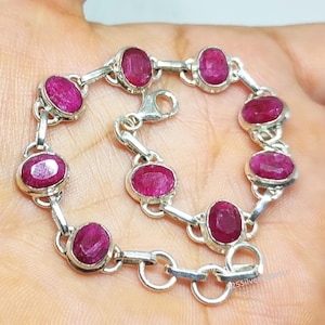 Pode incluir: Uma pulseira de prata com pedras preciosas ovais vermelhas escuras. As pedras são engastadas em biséis individuais e unidas por conectores de prata. A pulseira tem um fecho seguro. O design é elegante e atraente.