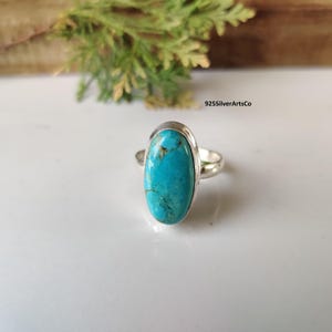 May include: A silver ring featuring a large, oval turquoise stone. The bright blue stone has brown and black veining. The ring is set in a silver band. The text "925SilverArtsCo" is visible in the background.