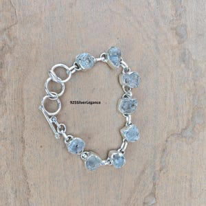 Könnte beinhalten: Ein silbernes Armband mit einer Reihe unregelmäßig geformter, hellblauer Edelsteine. Das Armband ist durch silberne Glieder verbunden und hat einen Verschluss. Der Text "925SilverLegance" ist sichtbar.