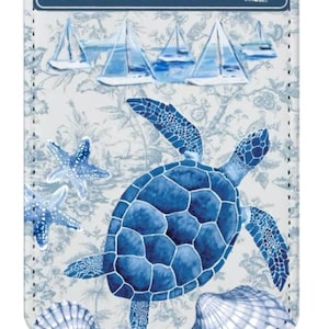 Peut inclure: Un porte-étiquette rectangulaire avec un motif côtier bleu et blanc. Il présente une tortue de mer bleue, des étoiles de mer et des coquillages. Le haut de l'étiquette indique "OCEAN BLVD". Le fond a des voiliers et un motif floral.