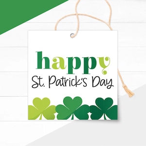 May include: A white square tag with the words "happy St. Patrick's Day" in green and black lettering. Three green shamrocks are at the bottom. A natural twine string is attached at the top.