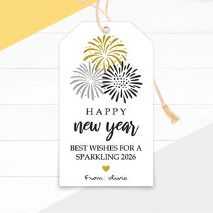 Puede incluir: Etiqueta de regalo blanca con temática de Año Nuevo. La etiqueta presenta ilustraciones de fuegos artificiales dorados, plateados y negros. El texto incluye "Happy New Year", "Best Wishes for a Sparkling 2026" y "From: olivia."