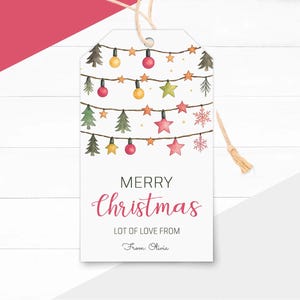 Pode incluir: Uma etiqueta de presente de Natal branca com um design em aquarela de luzes de Natal, estrelas e árvores. A etiqueta diz "MERRY Christmas" em uma fonte de script, com "LOT OF LOVE FROM" e um nome manuscrito abaixo. Uma corda está anexada.