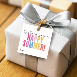 May include: A square white gift tag featuring the black text Wishing you a and the colourful text HAPPY SUMMER! in pink, yellow, blue, and orange, followed by the word From. The tag is attached with twine to a silver gift box wrapped in a silver ribbon.