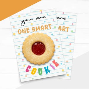 Op de afbeelding: Twee wenskaarten met een koekje en de woorden "you are ONE SMART COOKIE ART" op een witte achtergrond met blauwe lijnen en kleurrijke stippen. De koek is rond met een rood centrum.