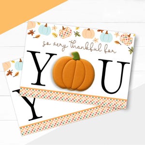 May include: Two white cards with the text "so very thankful for YOU". Each card features a large black "Y" and "U", with an orange pumpkin cookie in the center. The cards have a dotted border with fall colours and pumpkin and leaf illustrations.