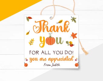 Può includere: Un'etichetta regalo quadrata bianca con le parole "Thank You" in arancione e giallo, una grafica di zucca e foglie autunnali. L'etichetta include il messaggio "For All You Do! You Are Appreciated" e un nome. Un filo di spago è attaccato.