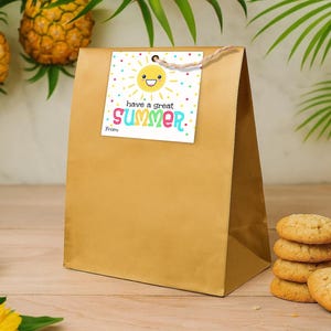 K&ouml;nnte beinhalten: Eine goldene Geschenkt&uuml;te aus Papier mit einem quadratischen wei&szlig;en Anh&auml;nger, der mit einer Schnur befestigt ist. Der Anh&auml;nger zeigt eine gelbe, l&auml;chelnde Sonne, bunte Konfettipunkte und den Text "have a great SUMMER" in bunten Buchstaben.