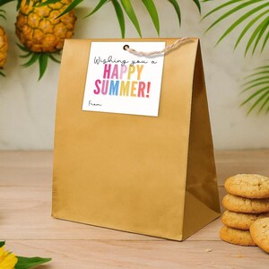 May include: A gold paper gift bag with a square white tag attached by a brown twine string. The tag features the black text "Wishing you a" and the colourful text "HAPPY SUMMER!" with the word "From" printed in black at the bottom left corner.