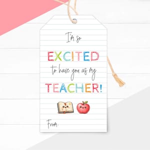 Pode incluir: Uma etiqueta de presente retangular branca com padrão de papel pautado e um cordão bege. O texto diz I'm so EXCITED to have you as my TEACHER! From: com letras coloridas e pequenas ilustrações de um livro aberto sorridente e uma maçã.