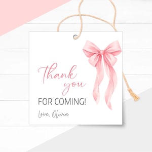 May include: A white square tag with a pink watercolor bow and the text "Thank you FOR COMING! Love, Olivia" in pink script. A natural twine string is attached at the top for hanging. The tag is designed for a party or event.