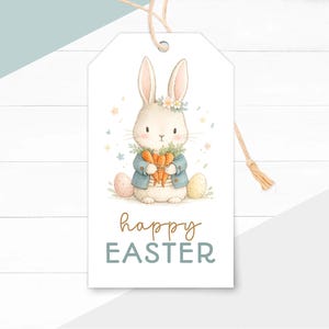 May include: A white gift tag with a watercolor illustration of a bunny holding carrots, wearing a blue jacket and a floral crown. Two Easter eggs are on either side of the bunny. The words "happy EASTER" are written on the tag.