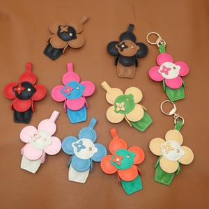 Peut inclure: Plusieurs porte-clés en cuir en forme de fleur, de couleurs variées : marron, noir, rouge, rose, bleu, vert et orange. Chaque porte-clés a un petit centre contrasté et une boucle d'attache. Certains ont des anneaux.