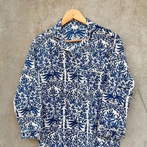 May include: A long-sleeve button-down shirt featuring a repeating dark blue floral and botanical pattern on a white background. The shirt has a notched collar, a single chest pocket, and white piping trim along the collar, pocket, and cuffs.