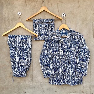 May include: A pajama set consisting of a long-sleeved button-down shirt and matching pants, featuring a repeating blue and white floral botanical print. The garments are displayed on wooden hangers against a textured gray wall surface.