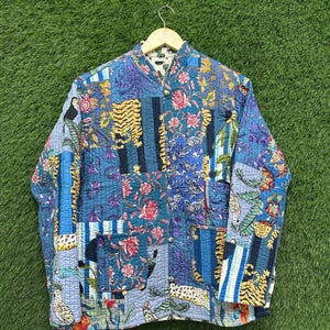 May include: A quilted jacket with a patchwork design. The jacket features a variety of patterns, including floral, tiger stripes, and geometric shapes, in shades of blue, teal, yellow, and pink. It has a mandarin collar and a button-up front.