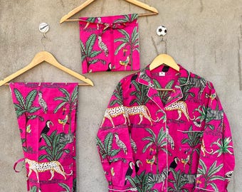 May include: A bright pink pajama set featuring a vibrant jungle print with leopards, toucans, and palm trees. The set includes a long-sleeved button-down shirt with a collar, matching trousers, and a folded fabric pouch, all displayed on wooden hangers.