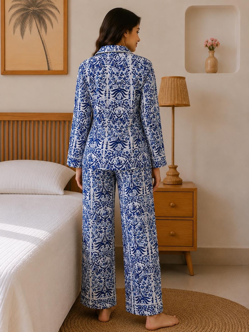 May include: A two-piece pajama set featuring a long-sleeved button-down shirt and matching wide-leg trousers. The fabric is white with a dense, intricate blue floral and botanical pattern, finished with white piping along the collar and cuffs.
