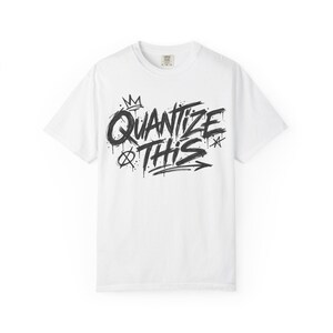 May include: A white short-sleeve t-shirt featuring a black graphic print on the chest. The design displays the text "QUANTIZE THIS" in a stylized, brush-stroke graffiti font, accompanied by small decorative elements including a crown and stars.