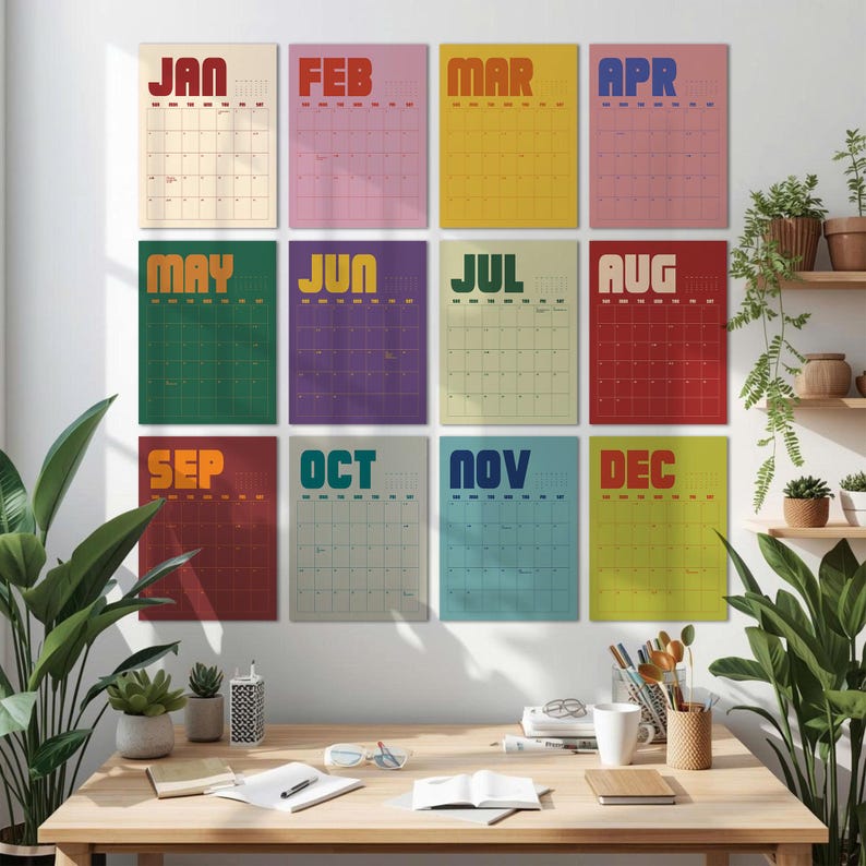 May include: A set of twelve monthly calendars, each with a different color background and month name. The calendars are displayed on a white wall above a wooden desk. The months are: Jan, Feb, Mar, Apr, May, Jun, Jul, Aug, Sep, Oct, Nov, and Dec.