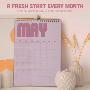 May include: A spiral-bound calendar for May, featuring a light purple background and bold, retro-style lettering. The calendar includes the text "A FRESH START EVERY MONTH" and "Bring joy and creativity to every new beginning."