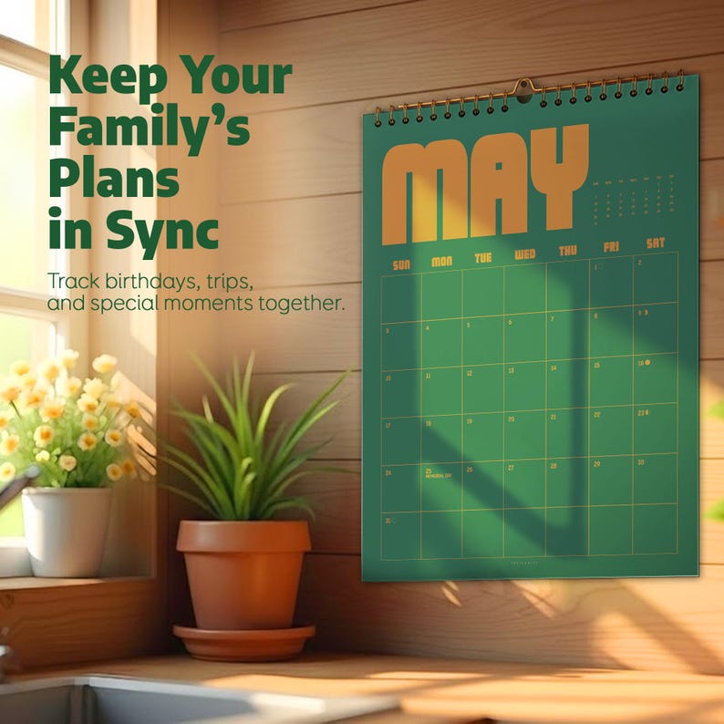 May include: A green wall calendar for May with gold lettering and a spiral binding. The calendar is hanging on a wooden wall. Text on the calendar reads "Keep Your Family's Plans in Sync".