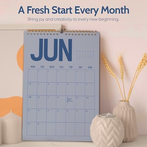 May include: A blue wall calendar for June with gold spiral binding. The calendar has a simple grid layout with the days of the week across the top. The text "A Fresh Start Every Month" and "Bring joy and creativity to every new beginning" are at the top.