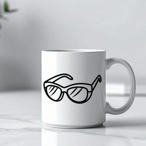 May include: A white ceramic mug with a black line drawing of sunglasses. The sunglasses are depicted with thick frames and lenses. The mug is on a white surface, with a plant and a blurred background.