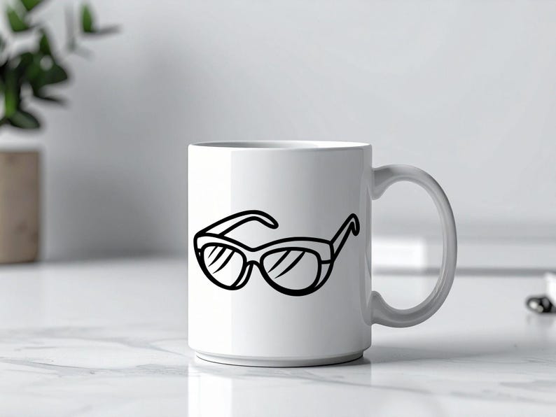 May include: A white ceramic mug with a black line drawing of sunglasses. The sunglasses are depicted with thick frames and lenses. The mug is on a white surface, with a plant and a blurred background.
