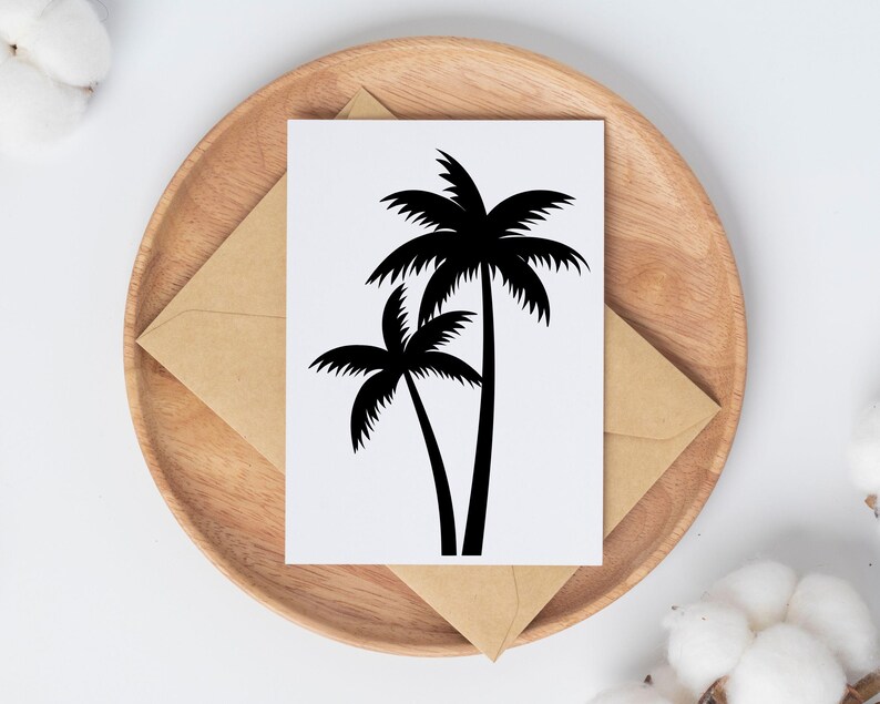 May include: A white card with a black palm tree design, placed on a wooden plate with a brown envelope. The palm tree illustration features two trees with detailed fronds. The background includes white and brown elements.