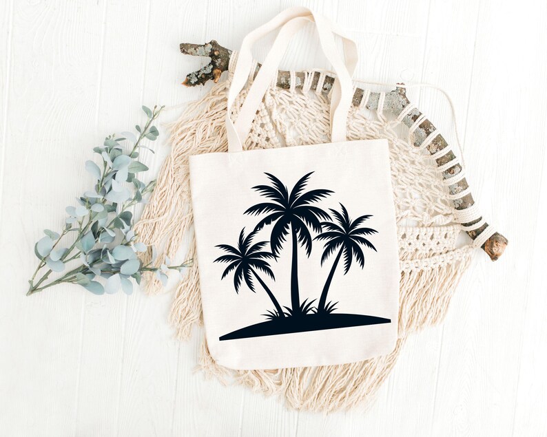 May include: Cream-colored tote bag featuring a black silhouette of three palm trees on a small island. The bag has two handles and is displayed on a white wooden surface with decorative elements.